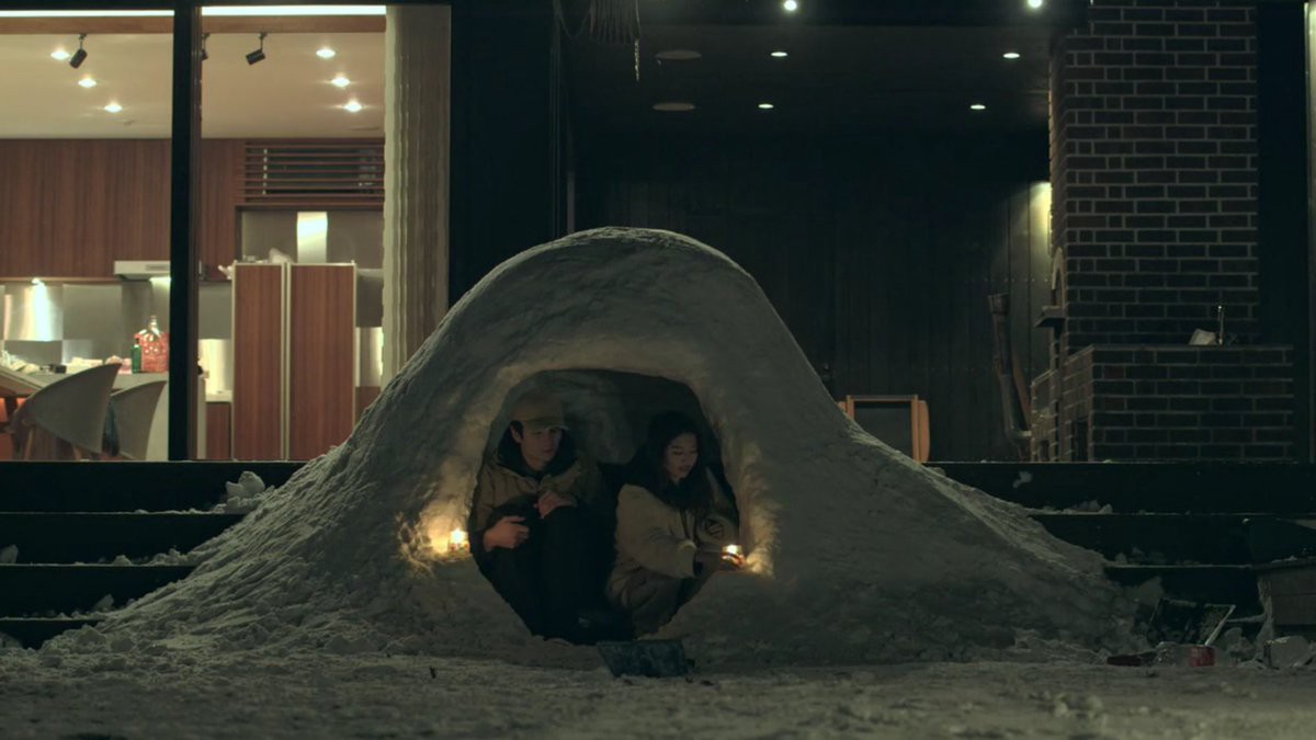 A man and a woman sit in an igloo in the front yard of Terrace House.