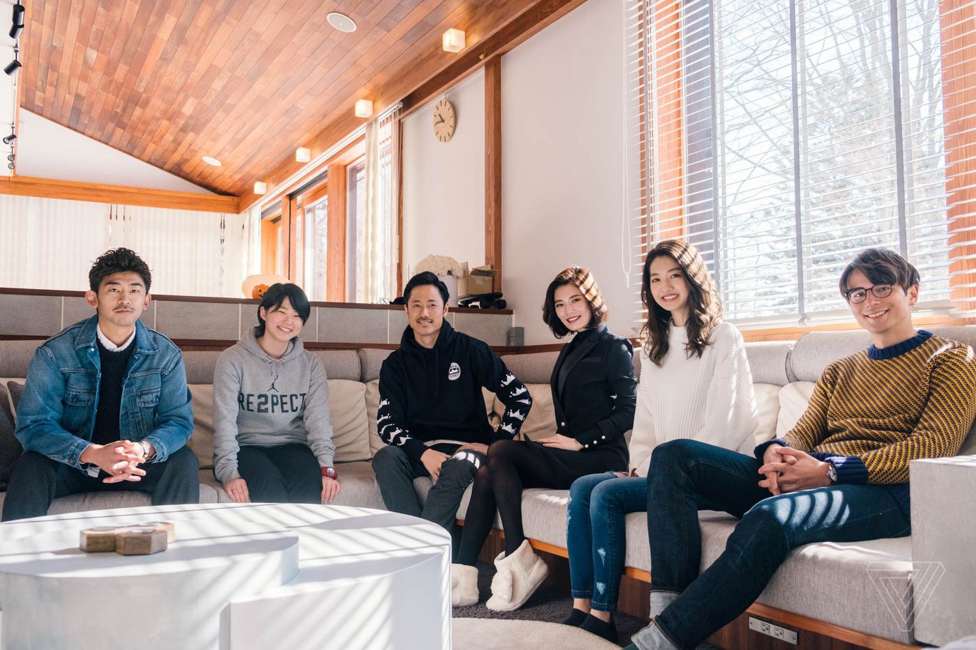 Six young adults sit in a spacious living room, smiling at the camera.