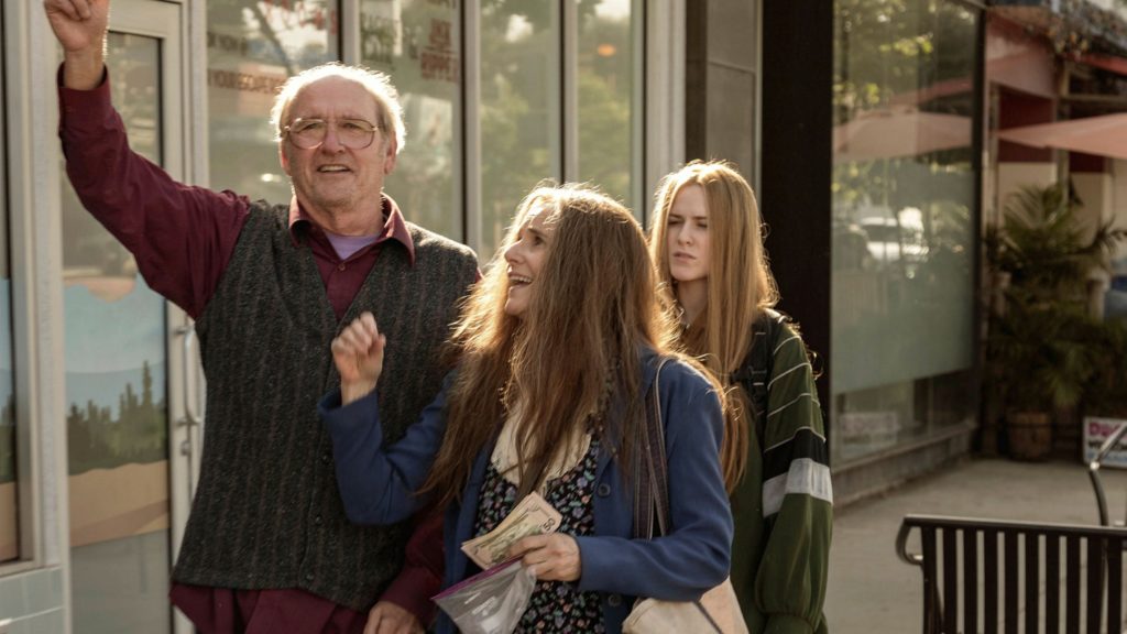 Robert, Theresa, and Old Dolio walk down a street. Robert and Theresa are cheering, and Theresa holds a stack of bills. Old Dolio looks uncomfortable.