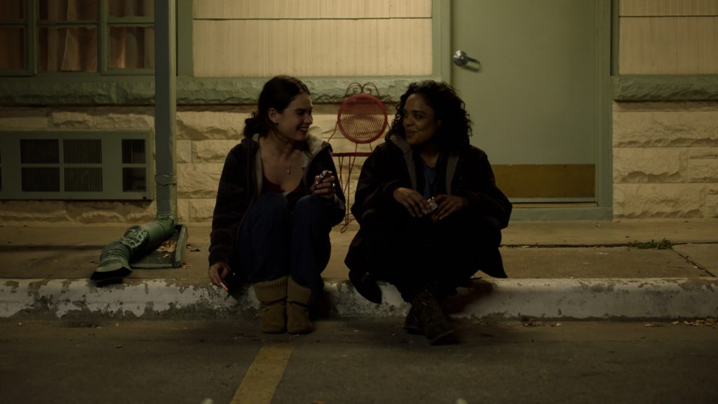 Deb and Ollie sit on the curb, talking and smiling.