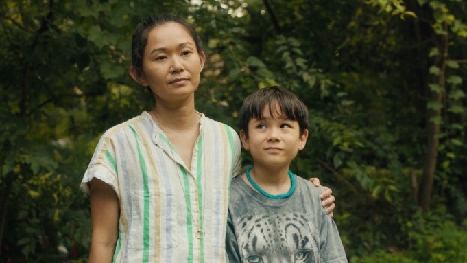 Kathy, a middle aged Asian woman, stands outdoors with her young son, Cody. She has her arm around his shoulder.