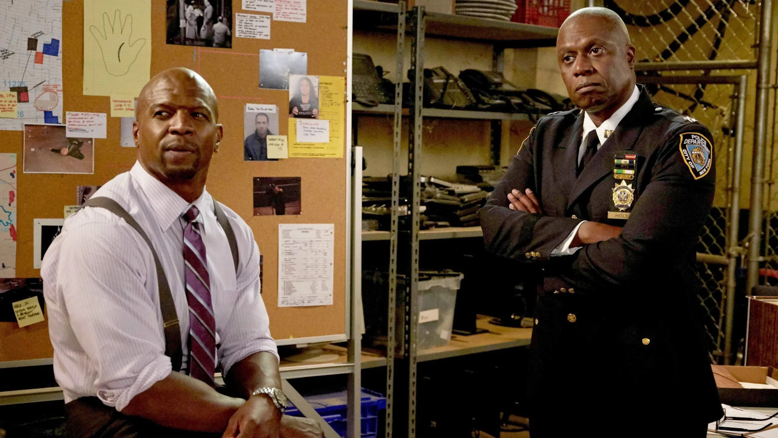 Terry and Holt, two Black police officers, in front of an evidence-filled cork board.
