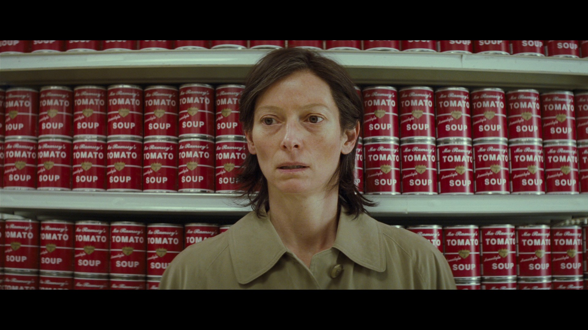 Eva (Tilda Swinton) sits in front of shelves full of canned tomato soup.