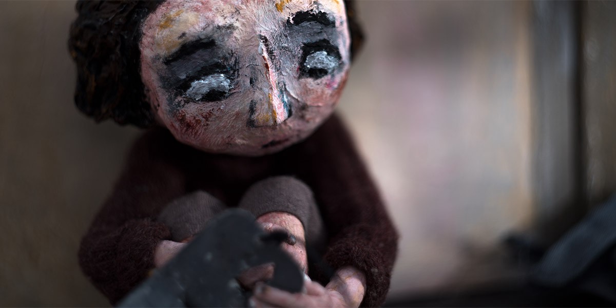 A paper mache doll of a young girl sits with her arms wrapped around her legs.