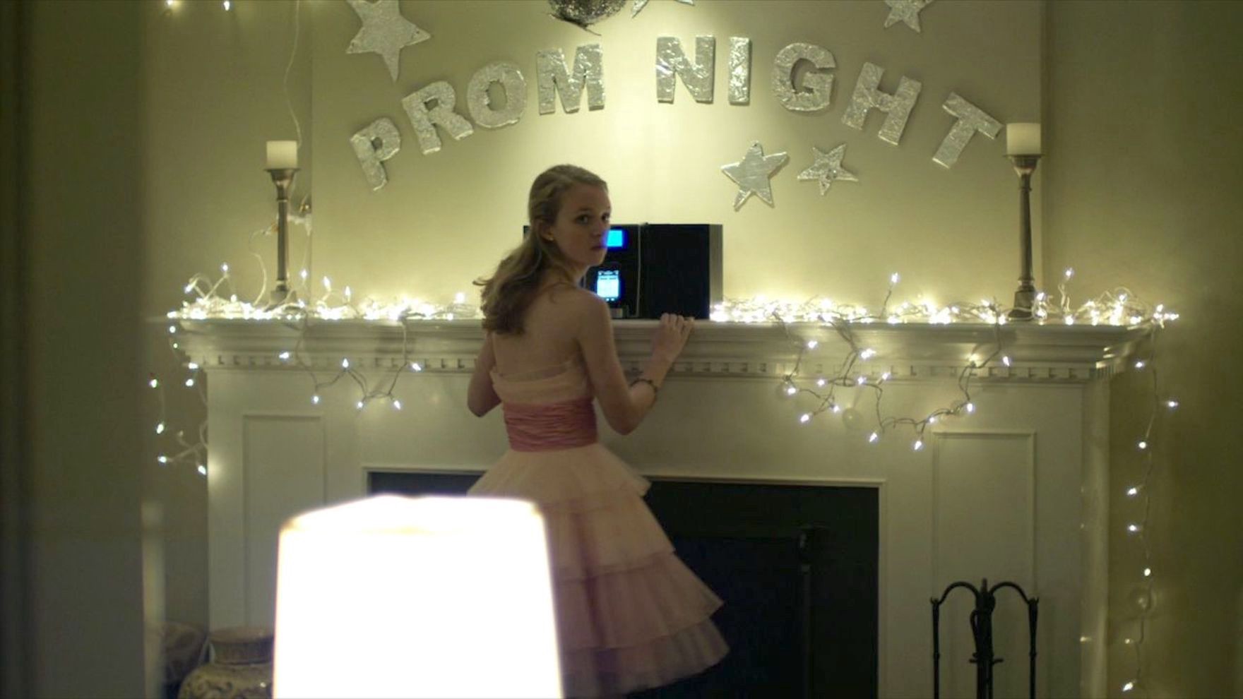 Jory, a teenage girl, stands in front of a laptop under a sign that reads "Prom Night." She's wearing a  prom dress.