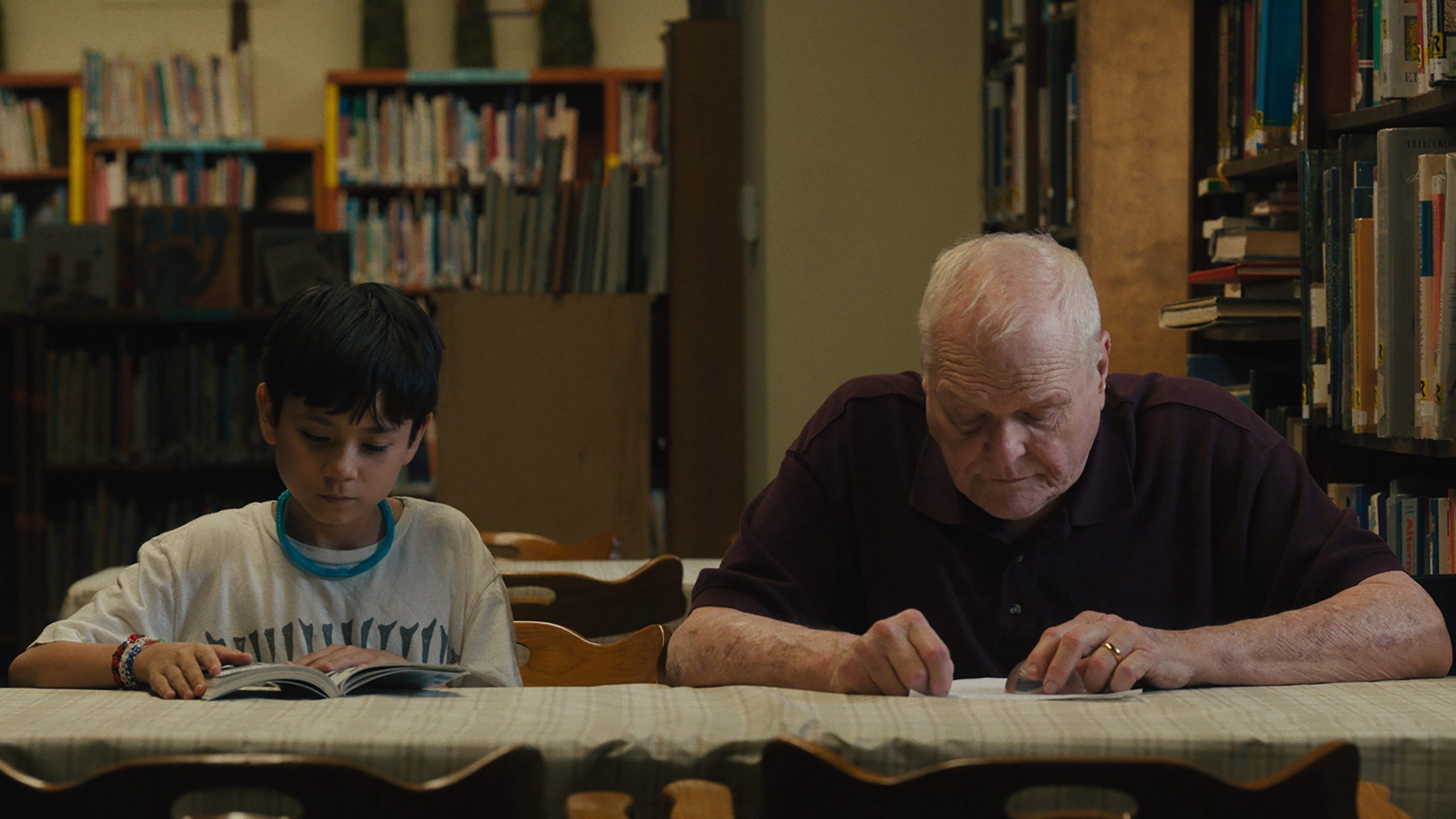 Cody and Del (an elderly white man) read together at a table.