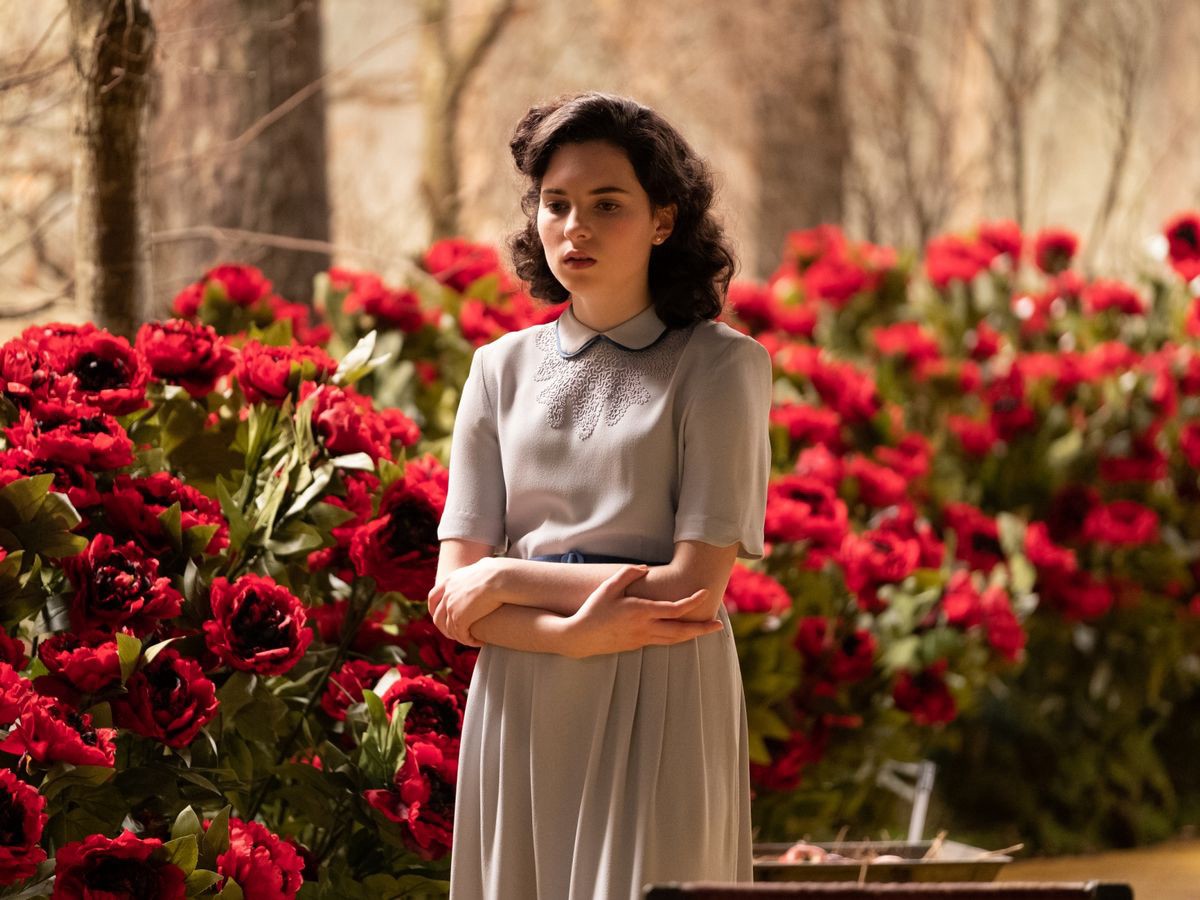 Darci Shaw as young Judy. She stands in front of a rose bush, arms crossed and looking slightly distraught.