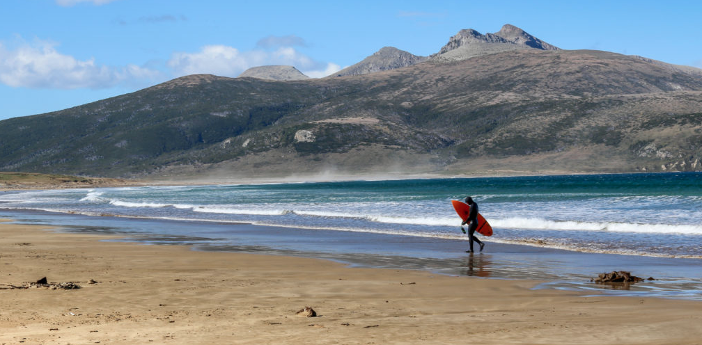 A surfer with a board under their arm walks along Argetina's Patagonian Coast
