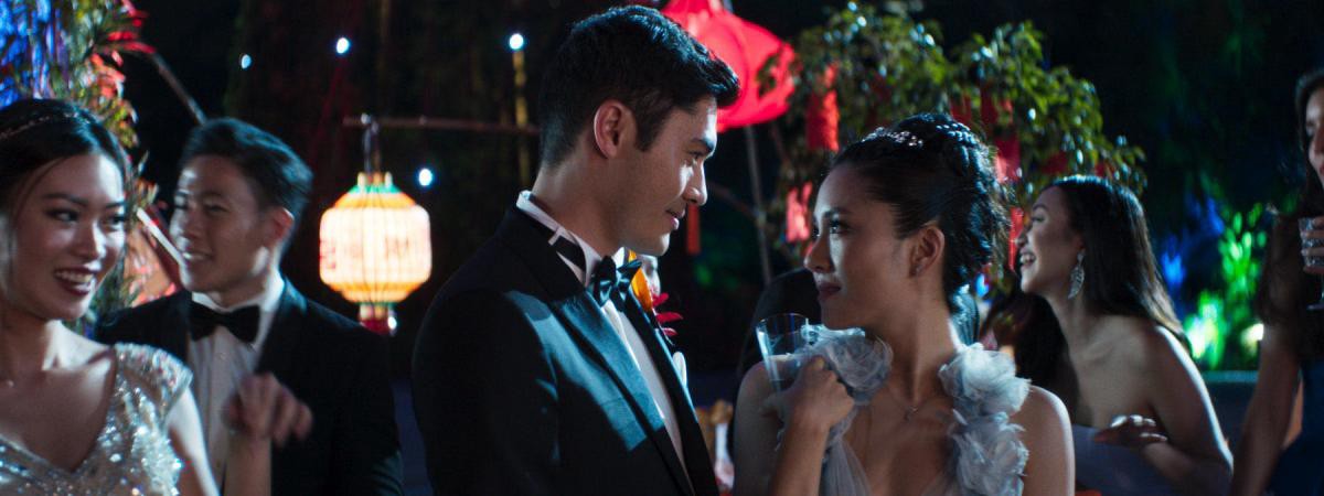 Nick (Henry Golding) and Rachel (Constance Wu) smile fondly at each other. They are dressed in evening wear and attending an outdoor party.