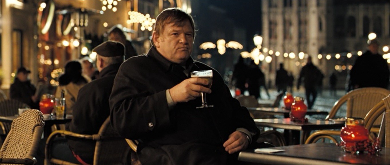 Ken (Brendan Gleeson) sips a drink at an outdoor table.