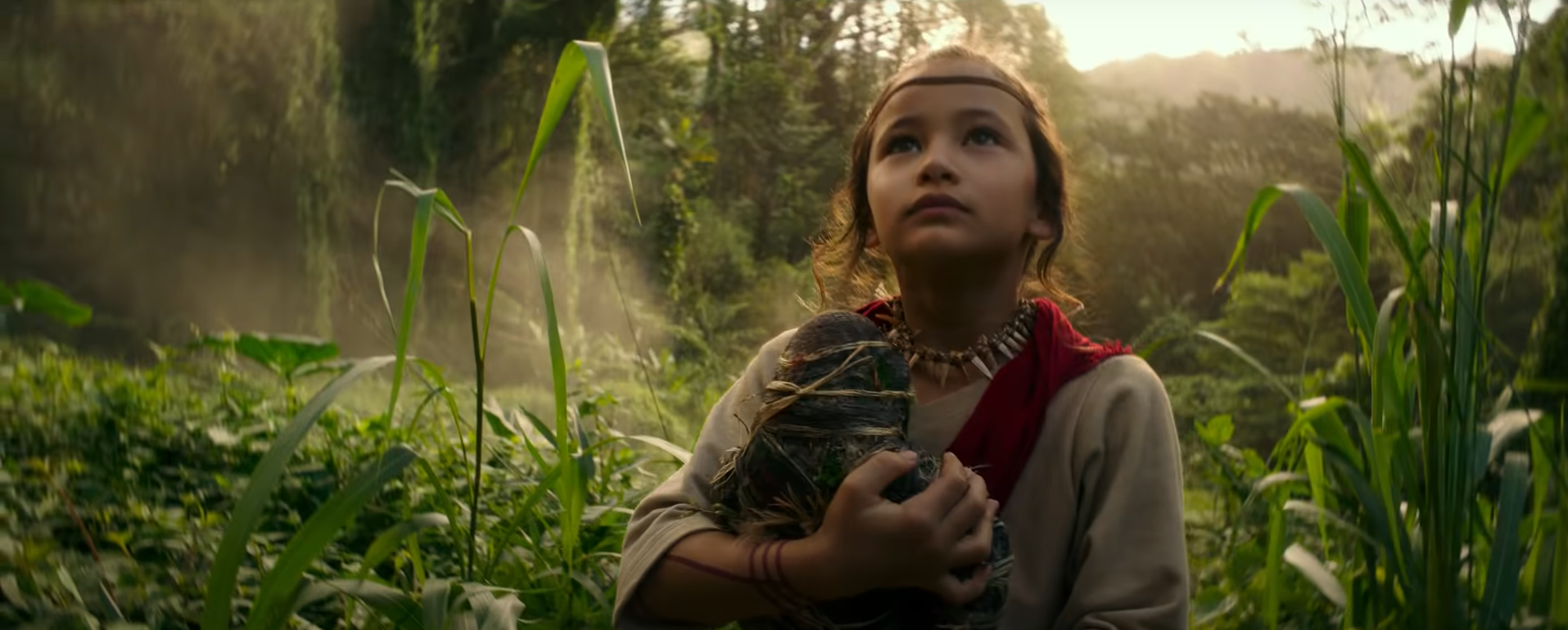 Jia (Kaylee Hottle), a young Indigenous girl holding a homemade Kong doll, stands in a jungle.