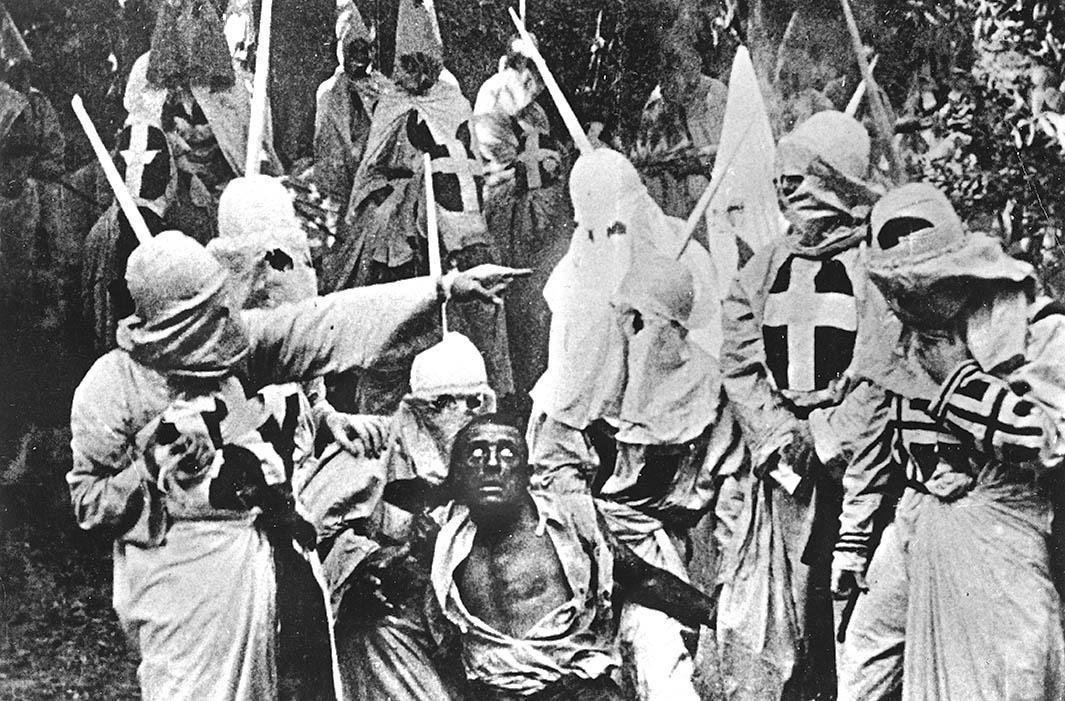 A screenshot from Birth of a Nation. A Black character (played by a white actor in blackface) is captured by hooded Klansmen.