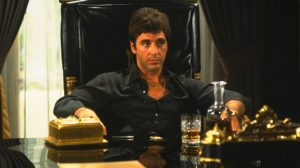 Al Pacino sits at a desk with a drink in front of him.