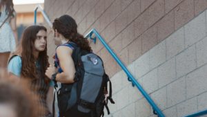 Anne and Clifton stand on the outdoor stairs of their school. Clifton steps closer to her in an attempt to intimidate the girl.