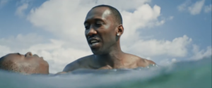 An older man is wading in the ocean with a young boy, helping him swim.