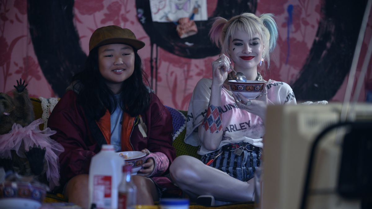 Cassandra Cain and Harley Quinn eat ceral together on a couch.