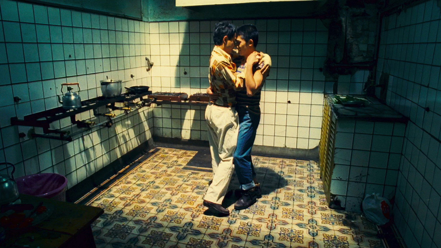 Two men slow-dance in a somewhat dilapidated kitchen.