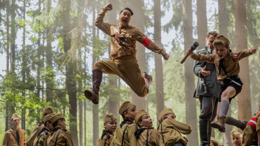 Jojo and Hitler leaping over the kids. Jojo is holding explosive.