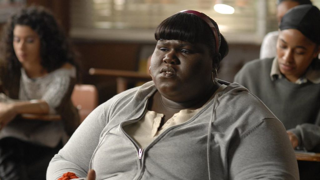 Precious (Gabourey Sidibe) sits at a desk in a classroom.