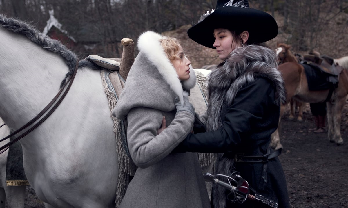 Kristina, wearing a furred jacket and a jaunty hat, helps Countess Ebba onto a horse.