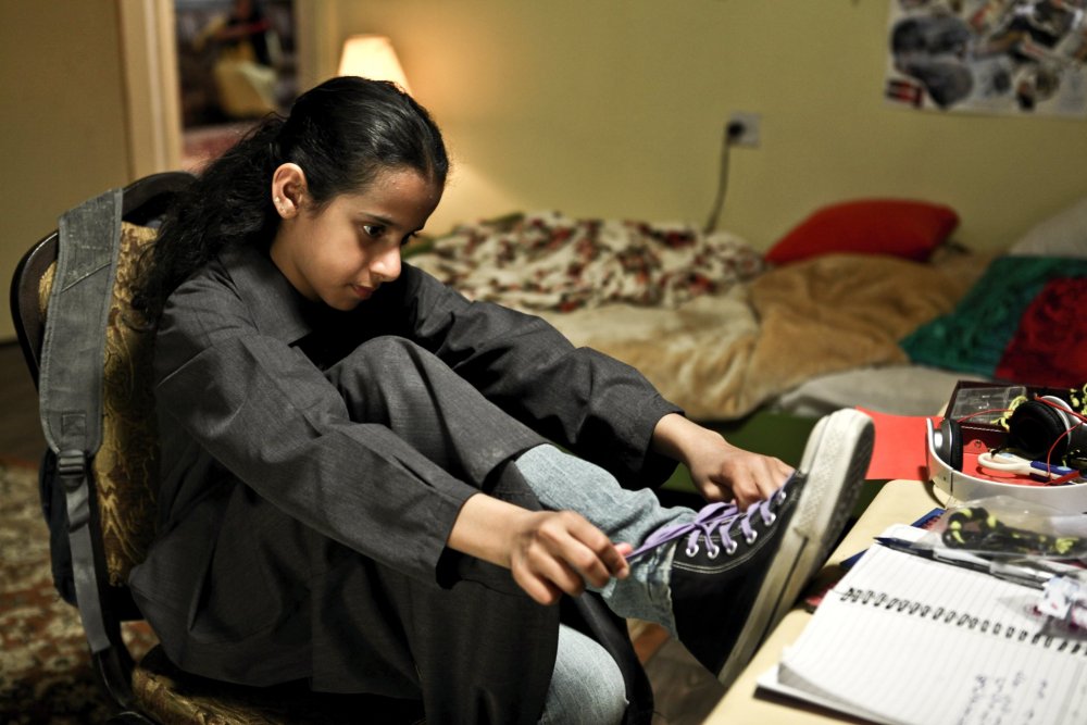 Wadjda in her bedroom, putting on her purple converse sneakers