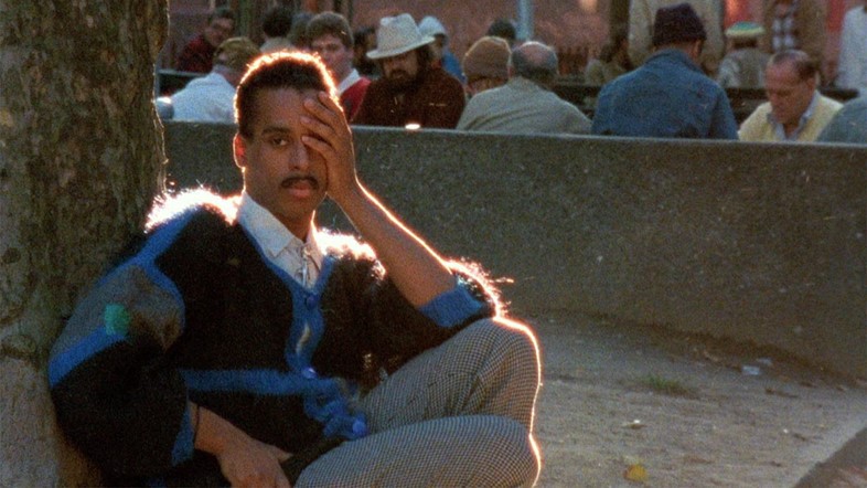 Willi Ninja, a well-known leader in the ballroom scene, sits with his back against a stone wall and a hand over his face.