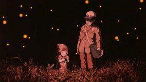 Setsuko and Seita standing in a field together with soft red lighting. They are surrounded by fireflies.