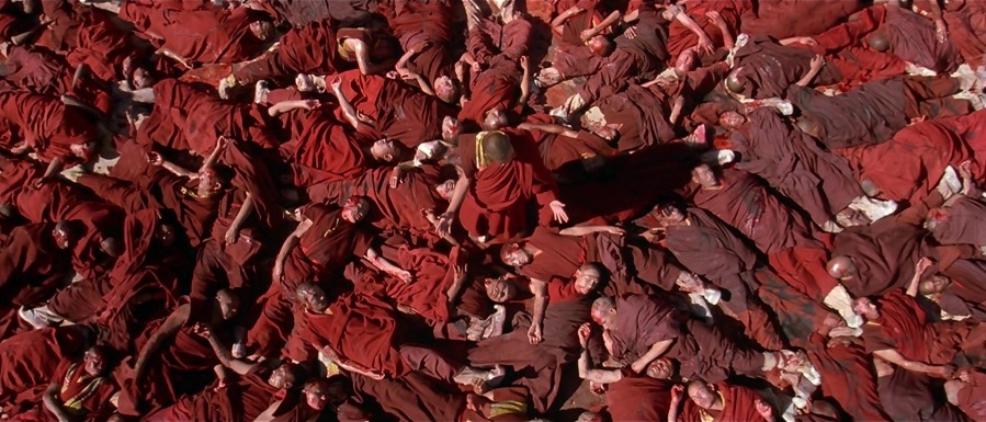 Tibetan monks wearing red robes, laying dead on the ground, Dalai Lama stands in center