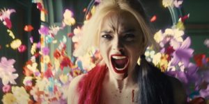 A still from "The Suicide Squad" of Harley Quinn screaming, flowers in the background