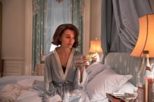 A still from "Jackie" of Natalie Portman as Jackie in her bedroom, sipping alcohol