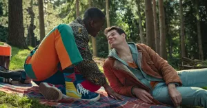 A still from Season 3 of Sex Education of Eric and Adam smiling on a picnic together
