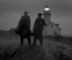 Two men walking outside with a lighthouse visible behind them.