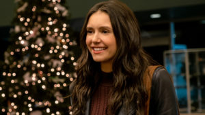 A still from 'Love Hard' of Nina Dobrev as Natalie smiling with a Christmas tree behind her