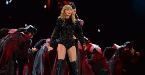 This image is of Taylor Swift on stage in her dazzling black outfit