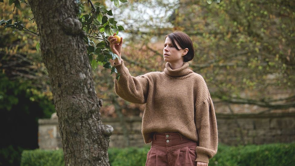 A woman wearing a chunky sweater reaches for an apple.