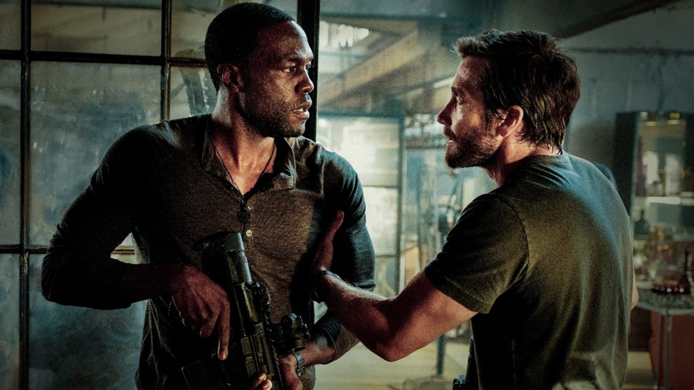 Yahya Abdul-Mateen on the left holding a gun and Jake Gyllenhall on the right holding the down his gun