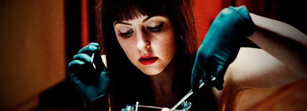 Close-up of Katherine Isabelle holding surgical scissors as she's stitching an unknown person.
