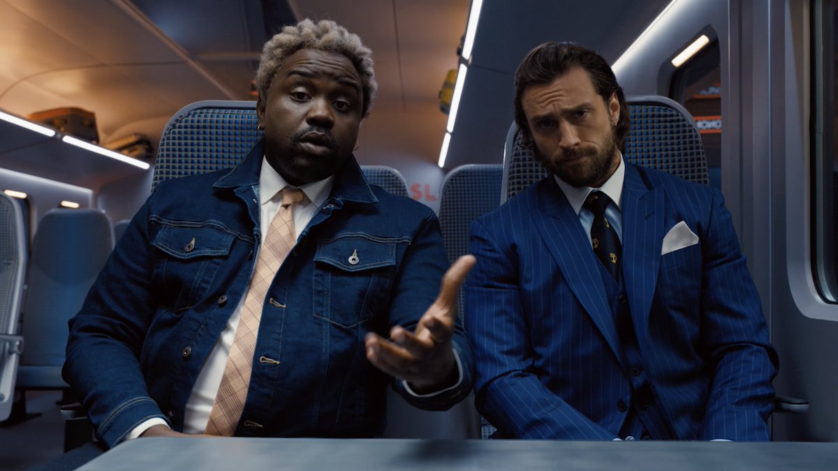 An image of the twin assassins Lemon and Tangerine sitting on the train dressed in matching blue suits looking at the camera curiously